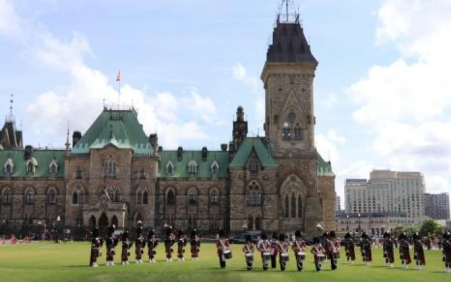 Ein Dudelsackorchester auf dem Rasen vor einem steinernen Regierungsgebäude in Ottawa